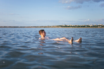 A man is resting on the dead sea. A man is swimming in a salt lake. A man with a beautiful figure swims in the water.