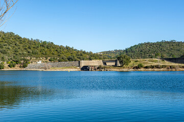 Dam lake of Saint-Cassien in Provence. The blue sky is reflected in the water. Partial view of the dam and the road leading to it.