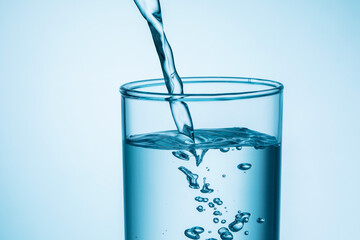 close up of pouring water into glass on blue background.