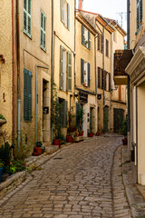Narrow street in a small Provencal village. The granite paving has shiny reflections. Some shop windows and their sign.