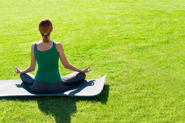 A woman practices yoga outdoors on the grass. Copy space