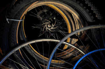 Old rusty bicycle wheels and tires in messy composition in dark room / space. 
