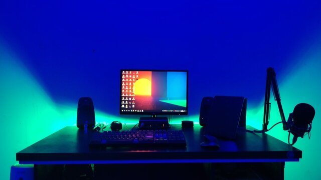 A desktop computer setup with colorful lights behind desk