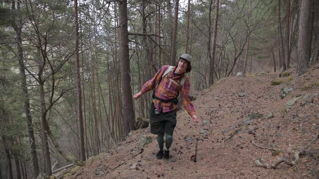 A young male traveler in a cap and with a backpack is a fun dancer in the evening forest. The concept of fun tourism in the mountains and good mood