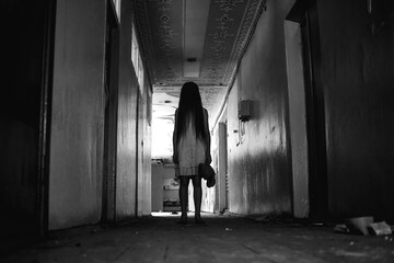 girl in a white dress with long hair and a Teddy bear in her hands stands in the middle of a creepy corridor in an abandoned building. Concept of horror, mysticism