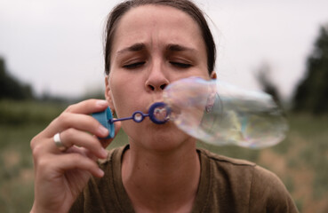 The girl blows soap bubbles. A young woman sits in nature and blows soap balls. The face in front.
