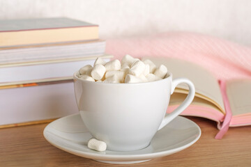 Fototapeta na wymiar White mug of cocoa with marshmallows on the desktop. A writing desk with books, an open notebook and a marshmallow mug. 