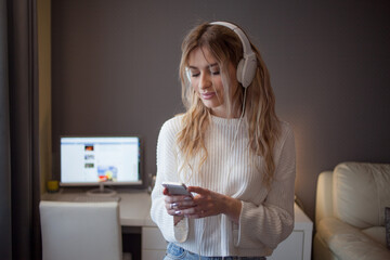 cheerful girl with a phone and large headphones listens to music on a subscription, surfs the...