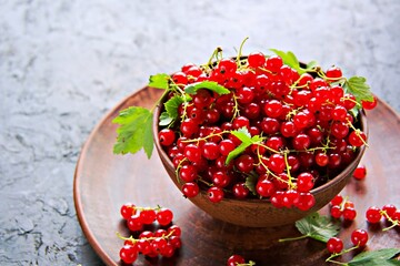 Fresh juicy berries of red currant in a clay bowl on a black concrete background.