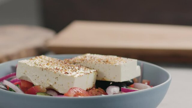 Slow motion slide of greek salad in blue bowl on kitchen countertop