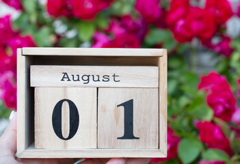 wooden block calendar present 1 and month august against a background of red rose bush