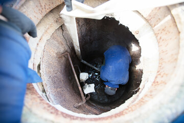 Worker cleans the sewer hatch.A worker cleans a sewer hatch. A man in the hatch. - obrazy, fototapety, plakaty