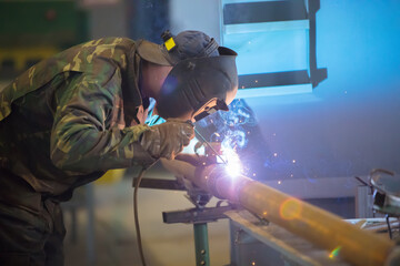 Welder at work. Man in a protective mask. The welder makes seams on the metal. Sparks and smoke when welding.