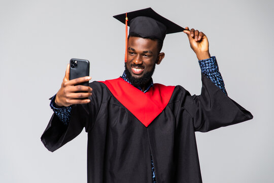 Young african man graduate in gown and cap take selfie isolated over white background