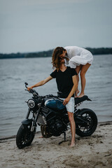 Fototapeta na wymiar Couple kissing on beach near motorcycle and water.