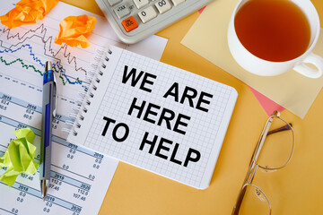We are here to help, is written on a notepad, on an office desk with office accessories.