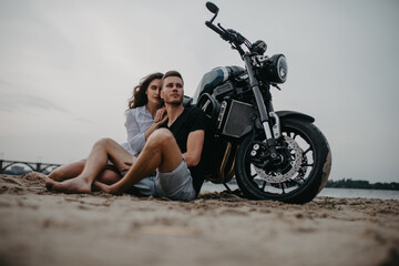 Obraz na płótnie Canvas Couple sits and hugs on beach near motorcycle.