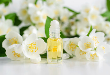 Obraz na płótnie Canvas Small glass roll-on bottle with essential jasmine oil (tincture, infusion, perfume) on the white background. Jasmine flowers close up. Aromatherapy, spa and herbal medicine ingredients. Copy space.