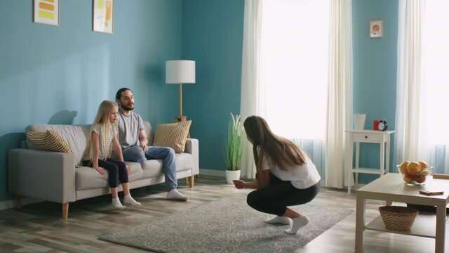 Parents are playing pantomime with their small daughter at home, mom is showing a word, dad and girl are guessing, all have fun together, happy family, Slow motion.