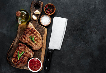 Two grilled beef steaks with spices served on a cutting board on a stone background with copy space for your text