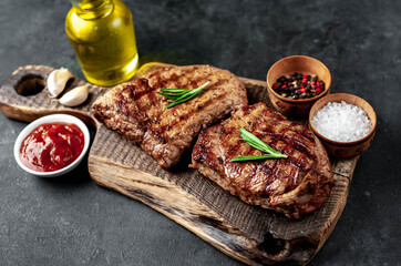 Two grilled beef steaks with spices served on a cutting board on a stone background