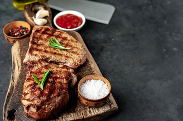 Two grilled beef steaks with spices served on a cutting board on a stone background with copy space for your text