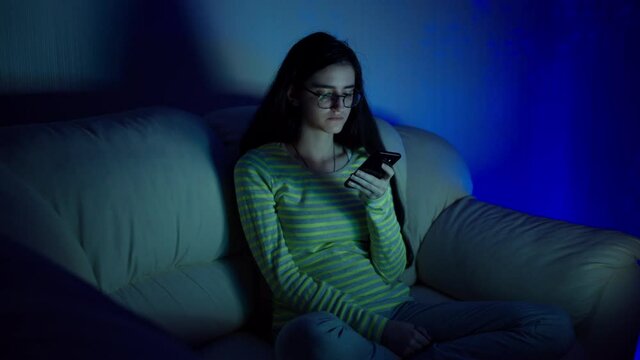 Late at night, a young brunette is sitting at the TV with a phone in her hands, camera movement