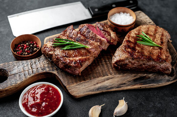 Two grilled beef steaks with spices served on a cutting board on a stone background