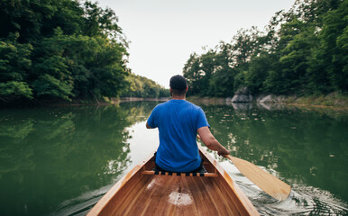 Rear view of man paddling canoe in the forest lake
