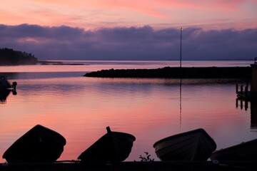 Three silhouettes of fishing boats in harbour. Sun is setting, and the water and sky are pink.