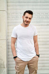 Men's street youth modern fashion. A young male hipste posing against a white roller shutter blinds. White T-shirt