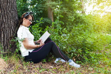 Young woman reading the book in the forest. Happy female smiling