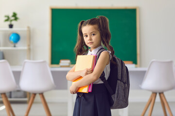 Back to school concept. Little girl schoolgirl with books in her hands is standing against...