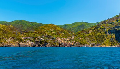 Fototapeta premium A panorama view along the Cinque Terre coast towards the village of Riomaggiore, Italy in the summertime