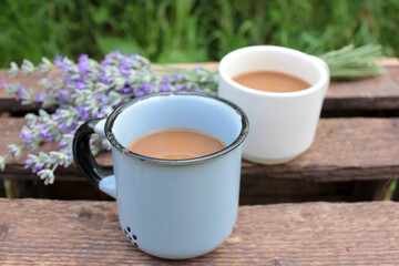 Two Cups of coffee with milk or cappuccino and lavender flowers on wooden board in summer garden. Enjoying morning coffee. Top view, copy space. Selective focus