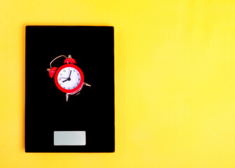 Red alarm clock on black scales on the yellow background. Time is money