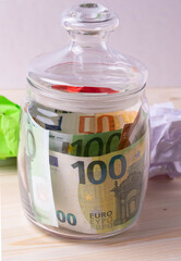 european paper banknotes of hundread euros in a jar on the white wooden desk as a concept of finance, currency rates or savings