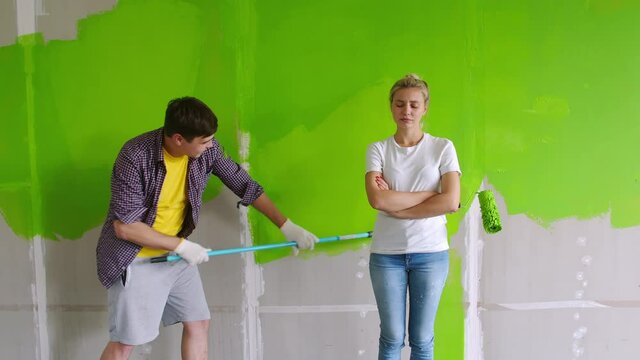 A young family is making repairs in a new apartment. A guy and a girl paint the wall of the house in green