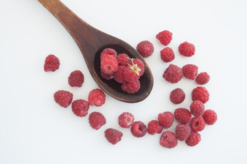 raspberry in an old wooden spoon and around it on a white background
