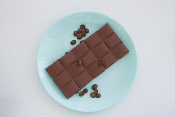 chocolate bar with coffee beans in light blue plate on a white background view from above
