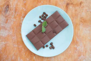 chocolate bar with coffee beans in light blue plate on a wooden background view from above
