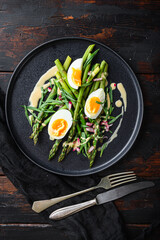 Asparagus with eggs and french dressing with dijon mustard, onion chopped in red vinegar  taragon on old dark wooden table, top view.
