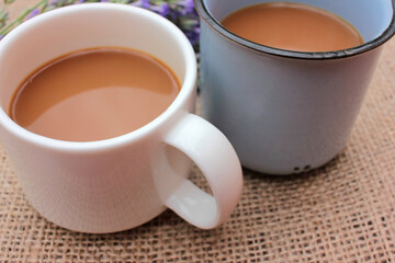 Two cups of coffee with milk or cappuccino and lavender flowers on burlap fabric texture. Enjoying morning coffee. Top view, copy space. Selective focus

