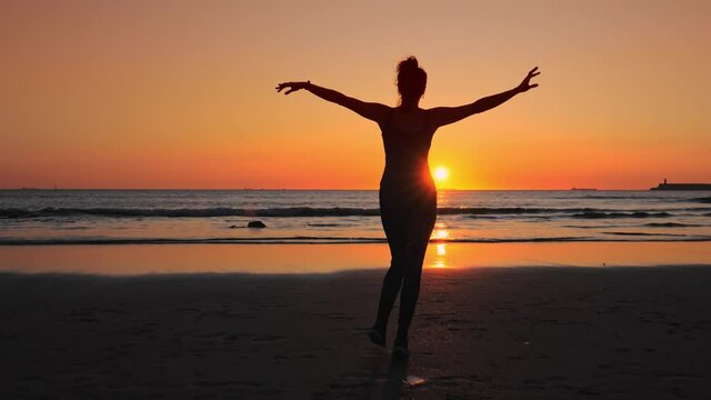 Happy woman in fitness clothes walking with arms raised up on the sand beach