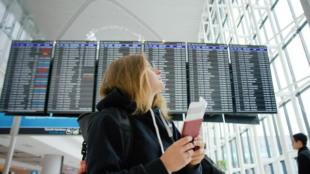 Young pretty woman with backpack wait for travel partner or couple with two flight tickets and passports. Excited for vacation or holiday. Worry not to miss flight. Airport scene, millennial traveler