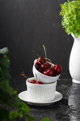 Selective focus, ripe cherries with water drops in a ceramic white Cup, on a dark background, vertical position