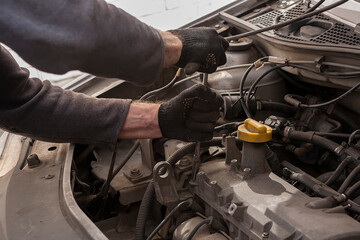 man's gloved hand repairs a car engine