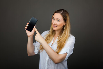 Naklejka premium Smiling woman is pointing on smartphone standing on grey background.