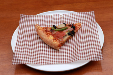 A piece of triangle Pizza  place on brown scotch paper  in the white round plate.