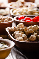 Peanuts in shell and dried fruits in bowls on wooden kitchen table